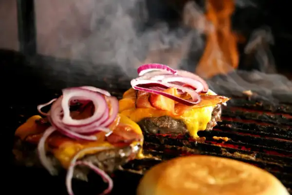 Pyszne burgery z grilla z roztopionym serem i czerwoną cebulą, parujące na ruszcie.