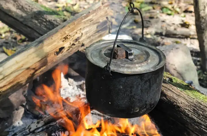 Czajnik wisi nad ogniskiem, gotując pyszne dania z ogniska. Płomienie tańczą pod garnkiem, tworząc magiczną atmosferę.